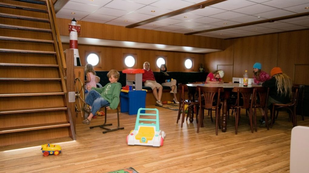 Children playing in a wooden-floored room with porthole windows and toy area.