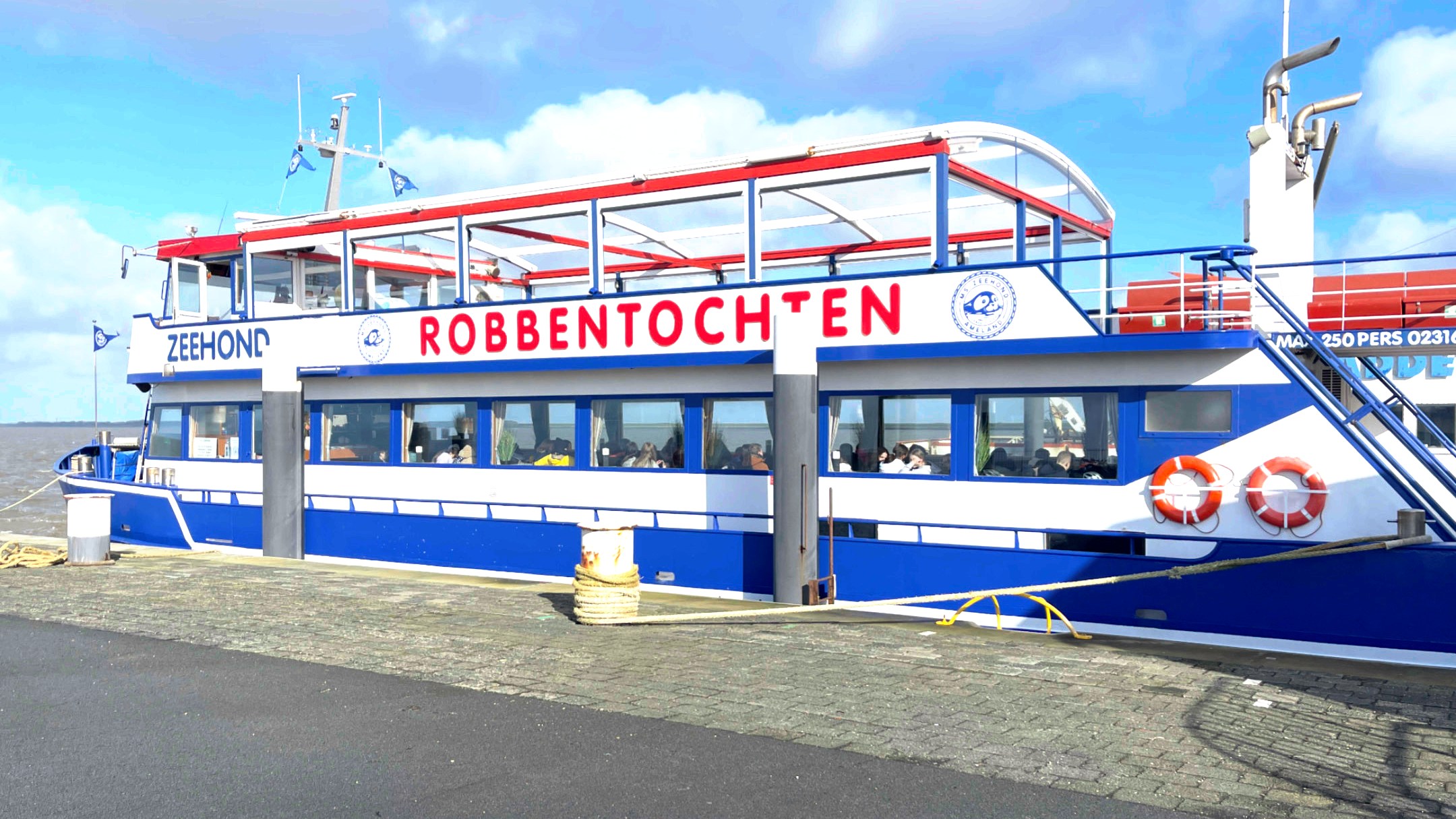 Blue and white boat named 'ZEEHOND ROBBENTOCHTEN' docked at a harbor, under a clear blue sky.
