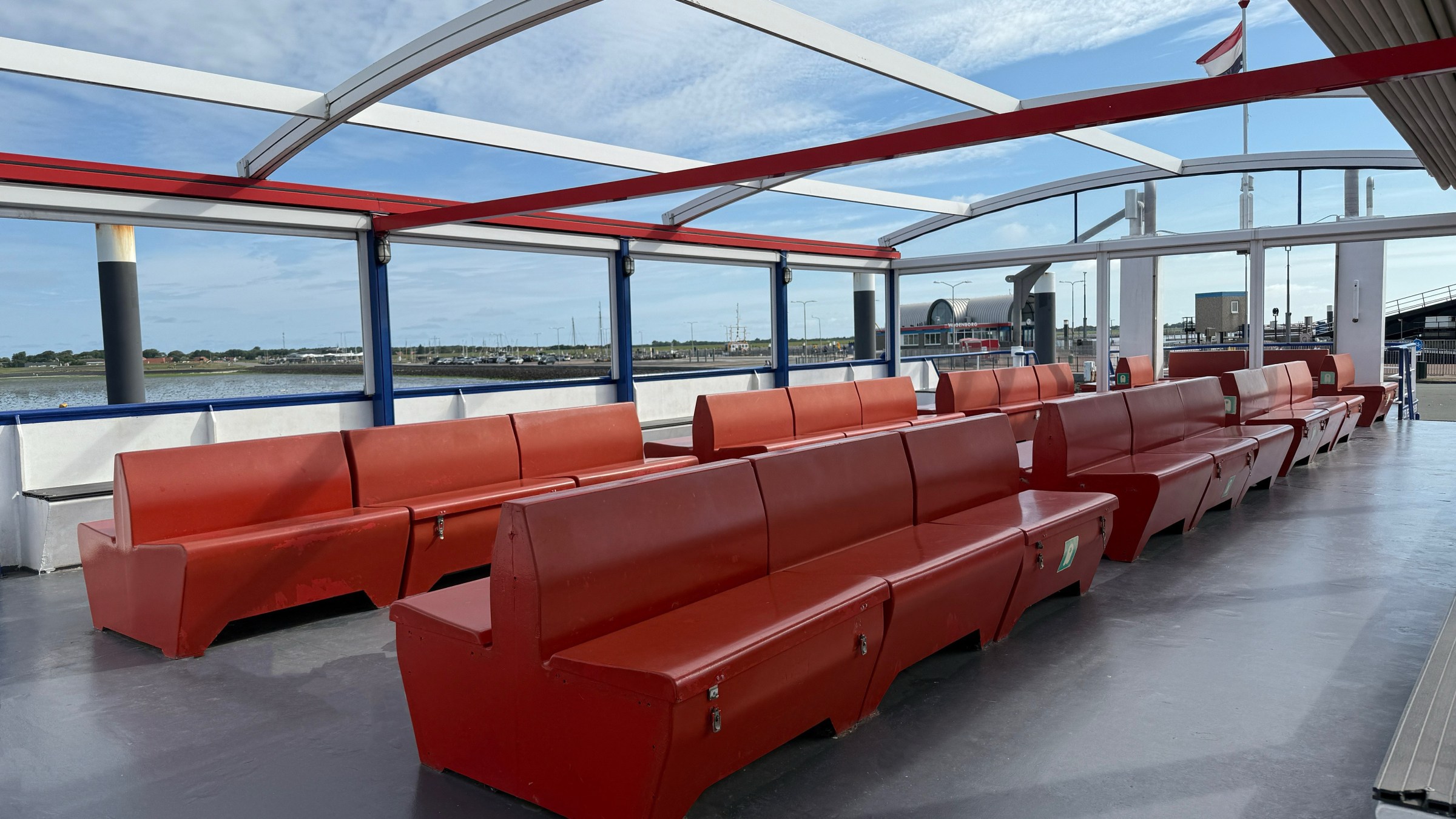 Empty red benches on a boat deck with blue open sky and waterfront view.