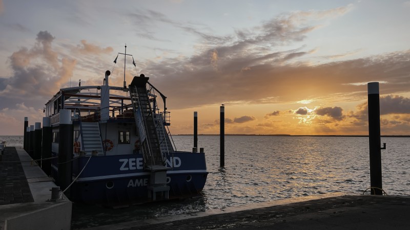 Boat docked at sunset with a cloudy sky and calm water in the background.