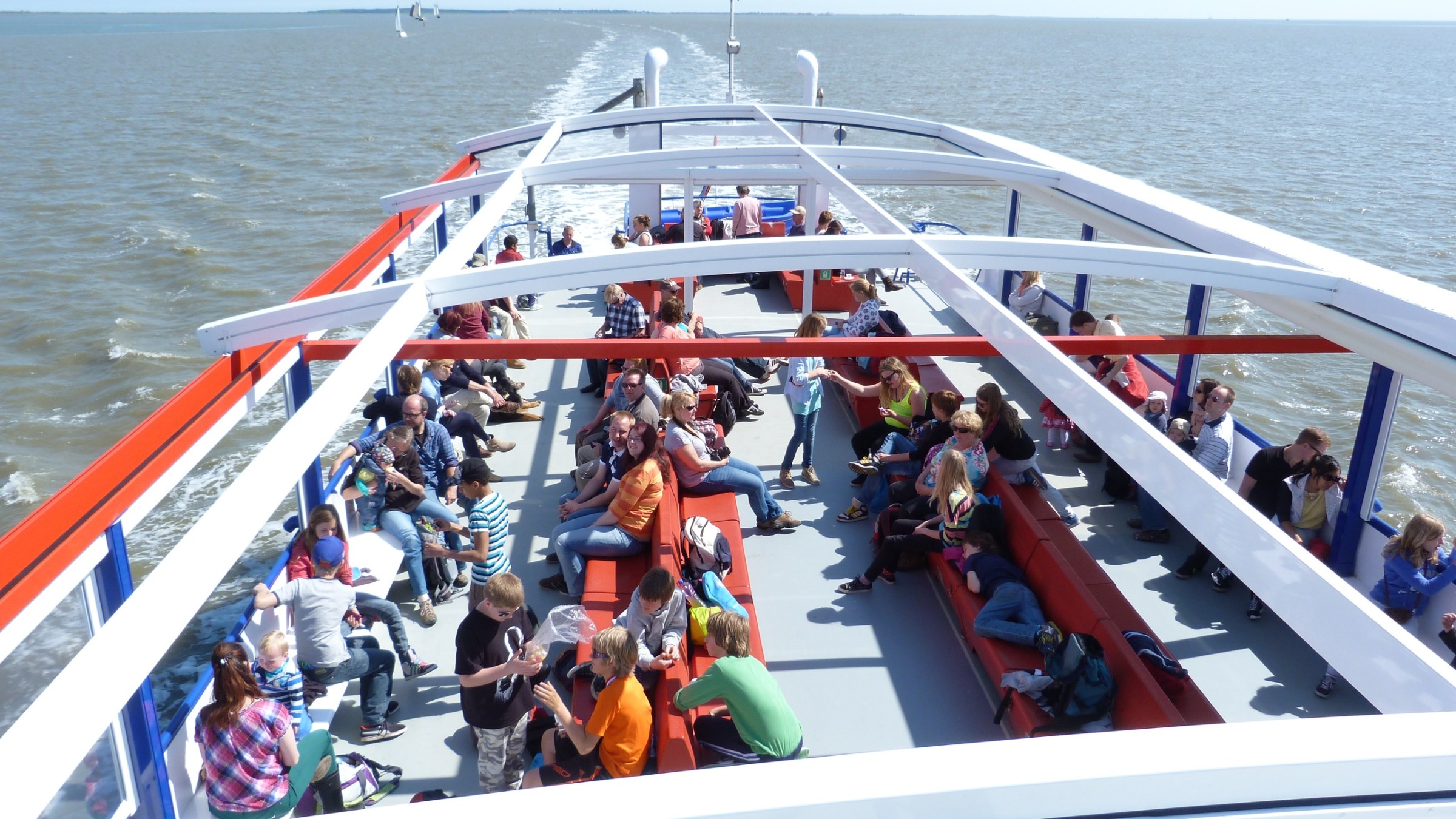People sitting on a ferry deck with benches under a clear blue sky.