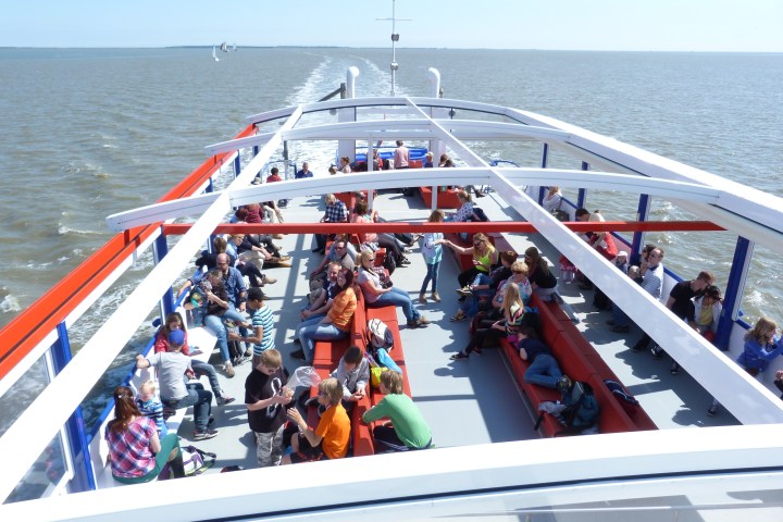 People sitting on a ferry deck with benches under a clear blue sky.