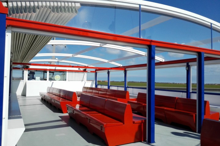 Open-top boat deck with red seats, blue pillars, and clear roof under a blue sky.