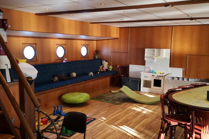 Spacious room with wood paneling, toys, a round table, and porthole windows on a ship.