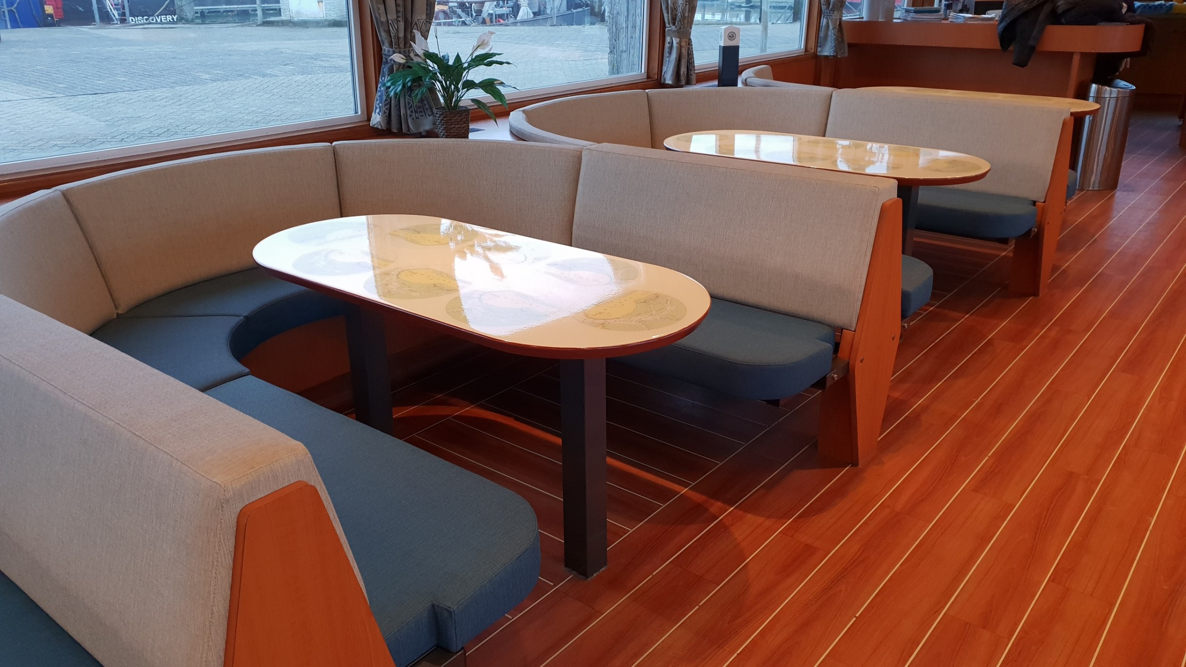 Interior with wooden floor, two curved sofa booths, and oval tables beside large windows.