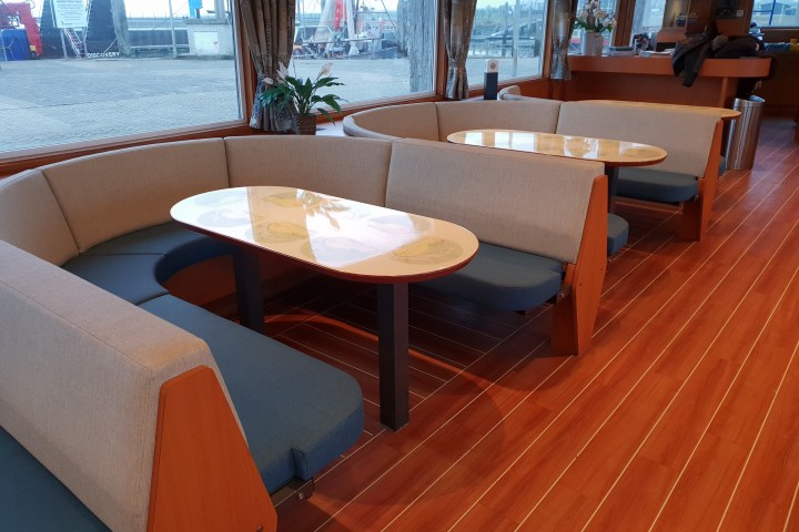 Interior with wooden floor, two curved sofa booths, and oval tables beside large windows.